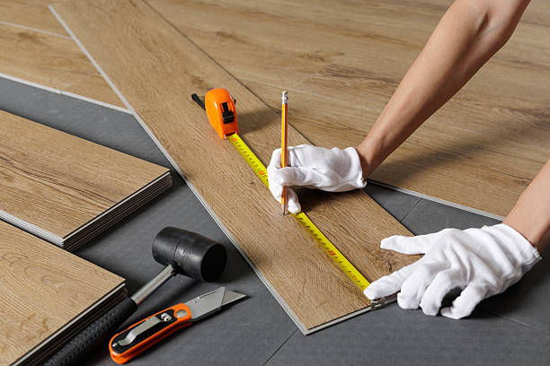 Close view of hands marking and measuring SPC vinyl plank on underlayment with tape and tools for home renovation